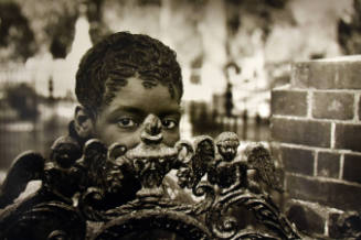 A girl peeking from behind an iron gate adorned with angels. 