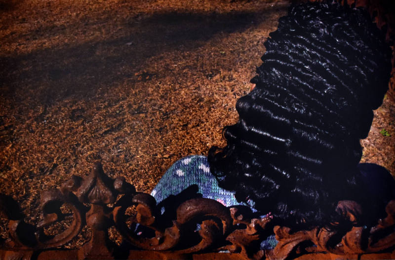 A towering wavy hairdo of a woman sitting against a rusty ornamented structure. 