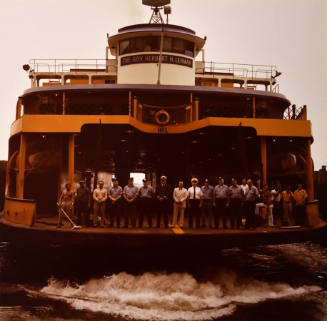 A group of people standing on the stern of a ferry boat.