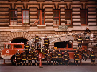 A group of firemen standing in front of a firetruck.