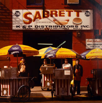 Four metal food carts with their attendants and yellow umbrellas. 