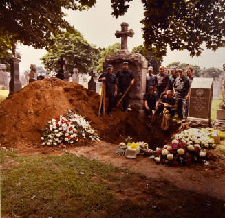 A group of cemetery workers standing behind an open grave.