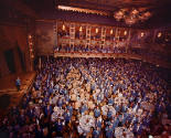 A sea of salesworkers standing around tables in front of a stage in a theater. 