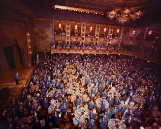 A sea of salesworkers standing around tables in front of a stage in a theater. 