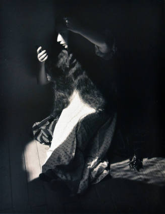 A black and white photograph of a woman sitting in partial shadow, holding a mirror and comb.