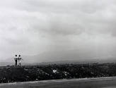 A black and white photograph of a couple walking along a road with mountains in the background.