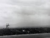 A black and white photograph of a couple walking along a road with mountains in the background.