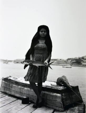 A black and white photograph of a young girl standing on a dock with a fish in her hands.