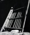 A black and white photograph of a dog sleeping under a wooden gate.