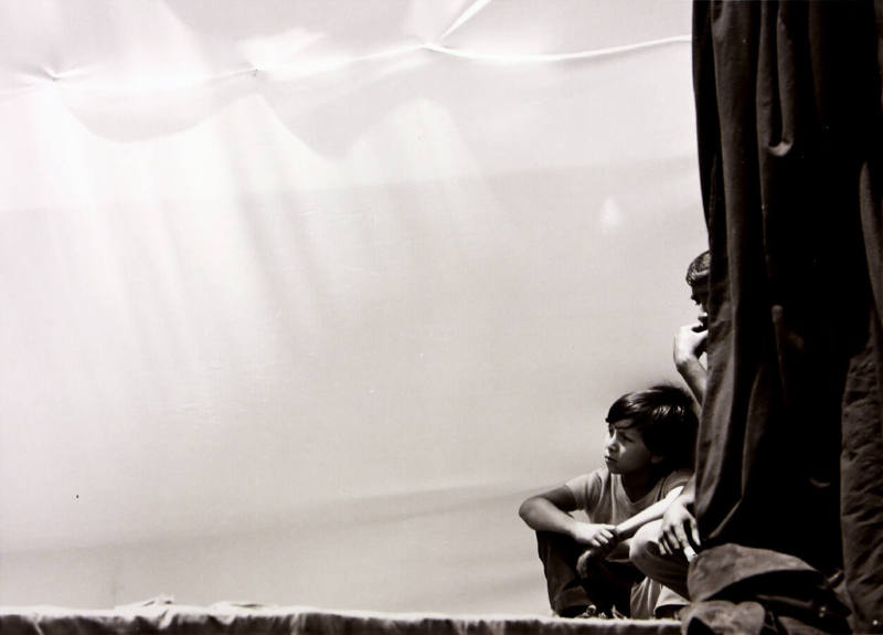 A black and white photograph of two boys sitting in front of a white cloth pulled taut but tuck…