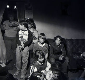 A black and white photograph of a group of children sitting and standing in a livingroom.