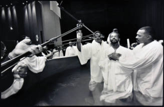 A black and white photograph of a man being baptized with microphones hovering over the baptism…