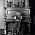 A black and white photograph of a little boy seated on a piano bench in front of a piano holdin…