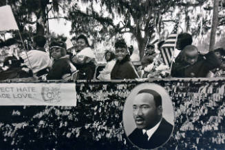A black and white photograph of children seated on a parade float with a painting of Dr. Martin…