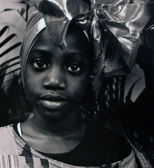 A black and white photograph of a girl with a metallic head wrap and an off-the-shoulder stripe…