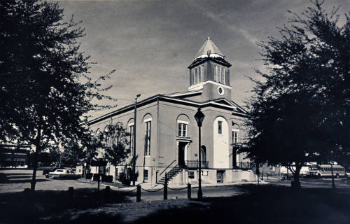 A black and white photograph of a corner of a church photographed from across the street, overl…