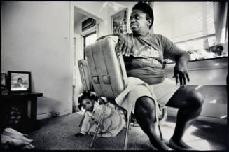 A black and white photograph of a woman seated on a chair with her head facing the left while a…