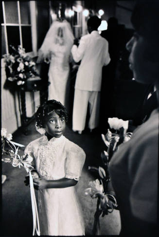 A black and white photograph of a girl holding flowers and looking at a partially photographed …