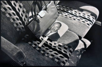 A black and white photograph of a bus seat with a pocketbook sitting on top of a fan with the i…