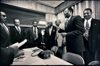 A black and white photograph of gentlemen in suits standing around a table signing.