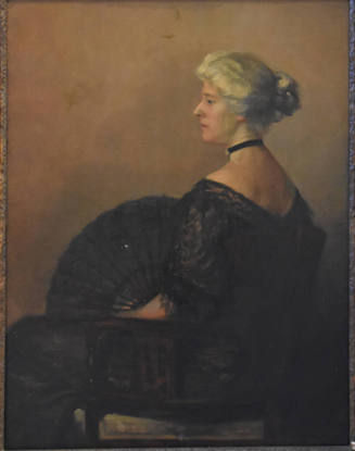 A seated woman wearing a black lace dress with matching fan.