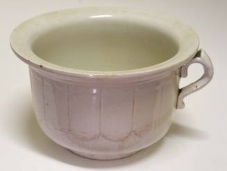 A white pot with a handle and imprinted design around the side.