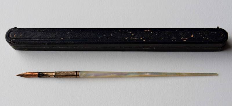 A pen with a carved brass nib attached to a mother-of-pearl handle in a hinged leather case lin…