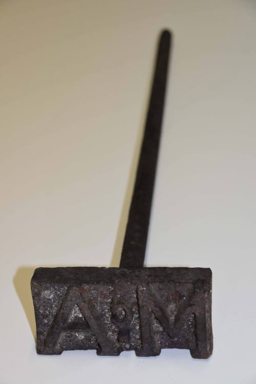 A branding iron with a rectangular head and wooden grip on the rod. 