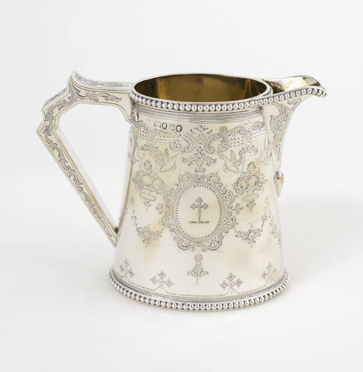 A Victorian sterling silver cream pitcher with a finely engraved cartouche depicting a heraldic…