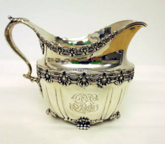 A sterling silver cream pitcher with four clawed-feet and floral gadrooning around the waist an…