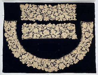 A set of floral lace collar and cuffs sewn to a piece of dark blue fabric for display.
