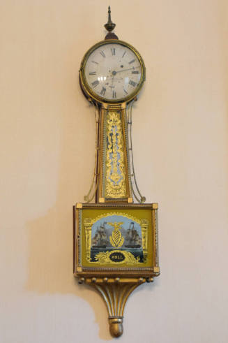 A mahogany banjo clock with brass fittings featuring a circular clock face over a pendulum colu…