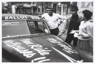 A black and white photograph of three figures conversing by the side of a car with text written…