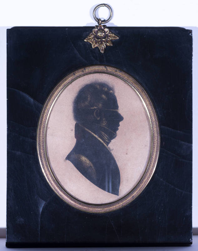 A drawn silhouette of a man in profile in an oval gilt frame with a lacquered wooden panel fram…