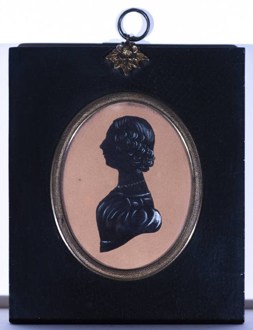 A drawn silhouette of a woman in profile in an oval gilt frame with a lacquered wooden panel fr…