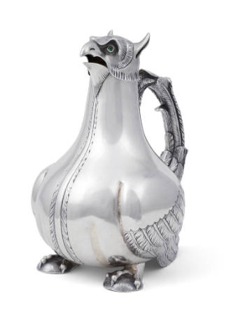 A silver claret jug in the form of a bird of prey with a feathered handle and emerald- colored …