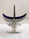 A silver oval sugar basket on a pedestal base with a cobalt blue glass liner and an engraved bo…