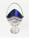 A silver oval sugar basket on a pedestal base with a cobalt blue glass liner and an engraved bo…