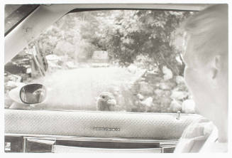 A black and white photograph of a woman sitting inside a car with her face turned from the view…