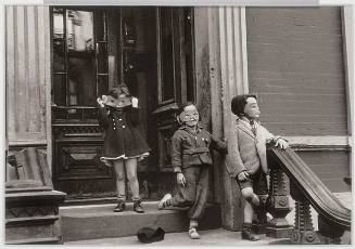 A black and white photograph of three children wearing masks standing on a stoop.