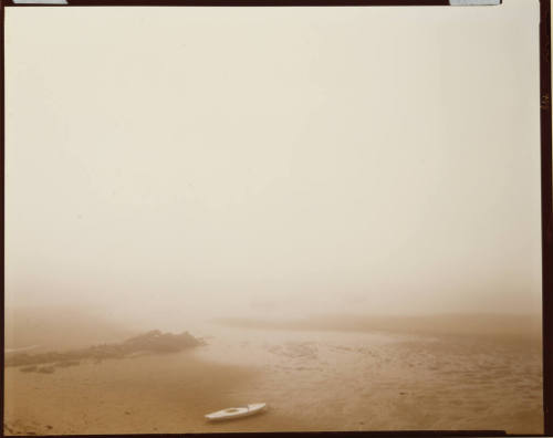 Misty landscape of a lone boat stranded on the sand during a low tide.