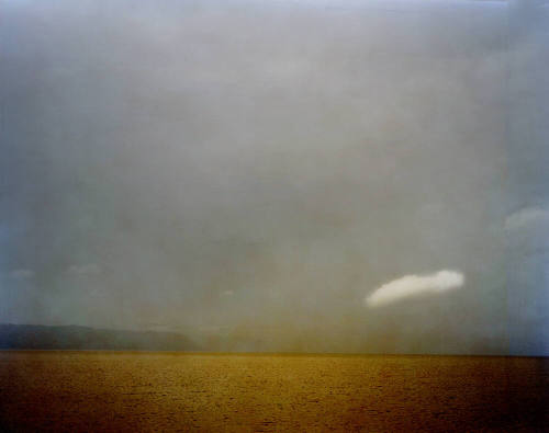 A cloudy sky over a golden river with mountains in the distance.