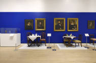 The east wall of the gallery hung with portraits above tables set with tea and coffee services.…