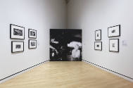 An installation shot of the south corner with a set of four photographs on either wall and a vi…