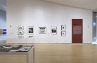 An installation shot of the "Travel" text panel with a series of photographs hung to the left. 