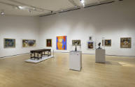 An installation shot of the Varnedoe gallery with two-dimensional works on the walls, two vitri…