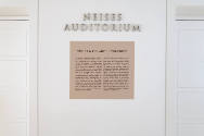 An installation shot of the "Tissot & the Art of the Print" text panel between the auditorium d…