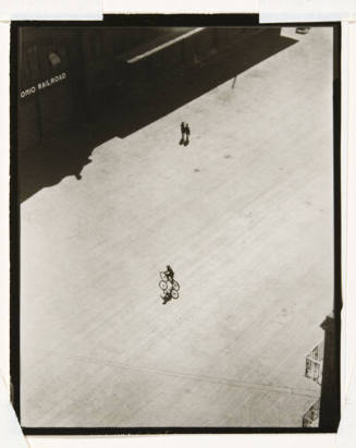 A bird's eye view of a bicyclist in the middle of the road and two figures walking on the top r…