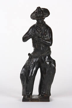 A bronze sculpture of cowboy rolling a cigarette. 

