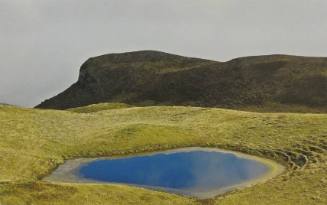 A color photograph of a lake surrounded by bright green hills in the Swiss Alps.

